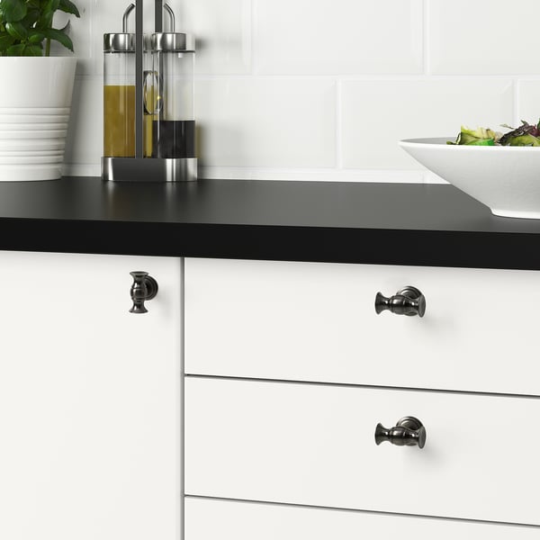 Modern kitchen with ANDERSFORS black knobs on white drawers, olive oil, and salad.