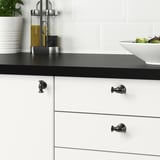 Modern kitchen with ANDERSFORS black knobs on white drawers, olive oil, and salad.