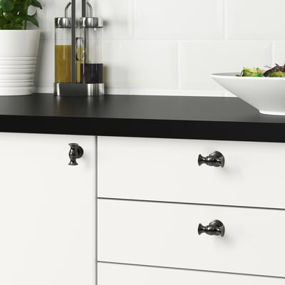 Modern kitchen with ANDERSFORS black knobs on white drawers, olive oil, and salad.
