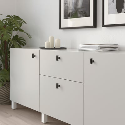 Modern living room with white cabinet, black handles, candles, magazines, and plant.