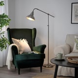 Green lamp lights dark green chair, cozy setup with mug, plant & couch.