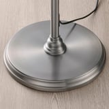 A sleek, brushed metal lamp base sits steadily on a wooden floor. The design is modern and sturdy, promising durability and elegance.