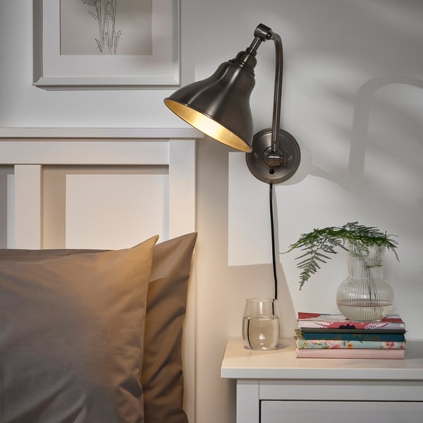 Brass ANKARSPEL lamp beside bed with nightstand items.