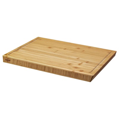 An ikea APTITLIG chopping board, light brown, made of bamboo with a groove on one side and slanted edges for easy grip.