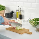Person chops onion on APTITLIG bamboo cutting board. Board has slanted edges for easy gripping and slicing. Knife and salad bowl are also visible.