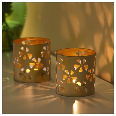Two gold-colored tealight holders with floral cutouts cast warm, patterned shadows on a surface.
