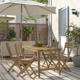 ASKHOLMEN wooden patio set with table, folding chairs, and cushions. Surrounded by fence and plants for cozy outdoor seating.