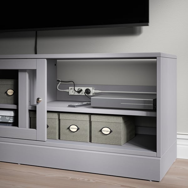 Tv stand with open shelves displaying ÅSKVÄDER power strips and storage boxes, showcasing organized and flexible power solutions.