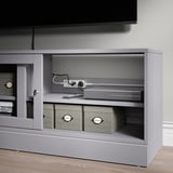 Tv stand with open shelves displaying ÅSKVÄDER power strips and storage boxes, showcasing organized and flexible power solutions.