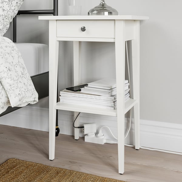 Small white nightstand with open shelf, books, phone, and adaptive power. ÅSKVÄDER series, bedsid.