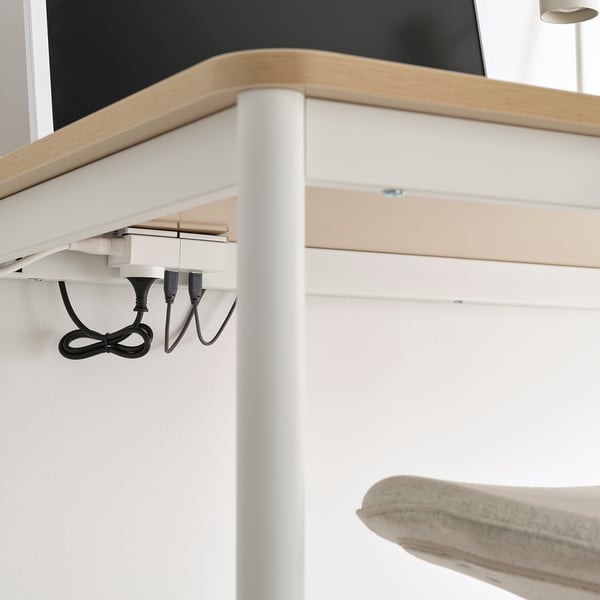 Under a wooden table, white cables with usb-a ports hang neatly, managing power supply efficiently. A light-colored chair is visible below.