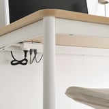 Under a wooden table, white cables with usb-a ports hang neatly, managing power supply efficiently. A light-colored chair is visible below.