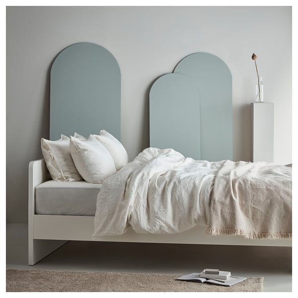 Minimalist bed with teal arched headboard, white linens, and books.