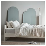 Minimalist bed with teal arched headboard, white linens, and books.