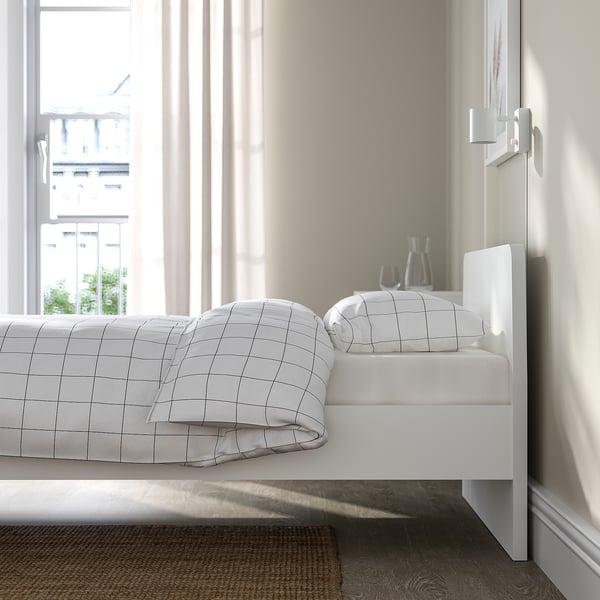 A modern white bed frame with low headboard, positioned under a window. It adjustable bed sides, allowing for varied mattress thicknesses.