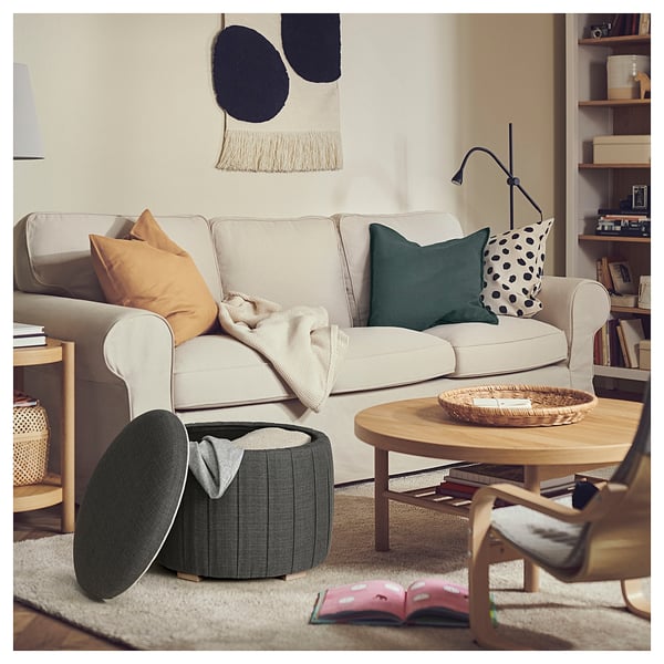 Cozy living room with beige sofa, wooden coffee table, and green storage ottoman. Colorful pillows add warmth.