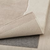 Image shows corner of thick, beige, handmade wool rug with visible texture detail.