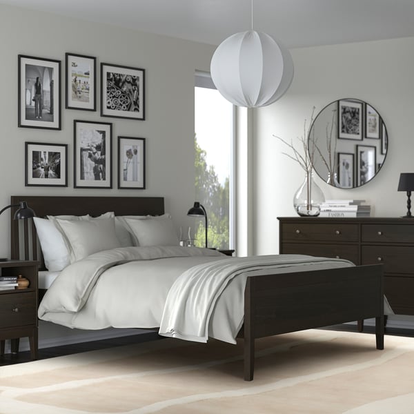 Modern bedroom with black furniture, grey rug, white decor, round mirror, light blanket, large window.