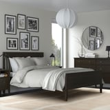 Modern bedroom with black furniture, grey rug, white decor, round mirror, light blanket, large window.