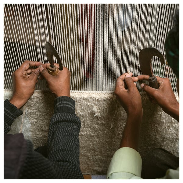 Hands weaving wool rug on loom, creating intricate pattern. Traditional craftsmanship in progress.