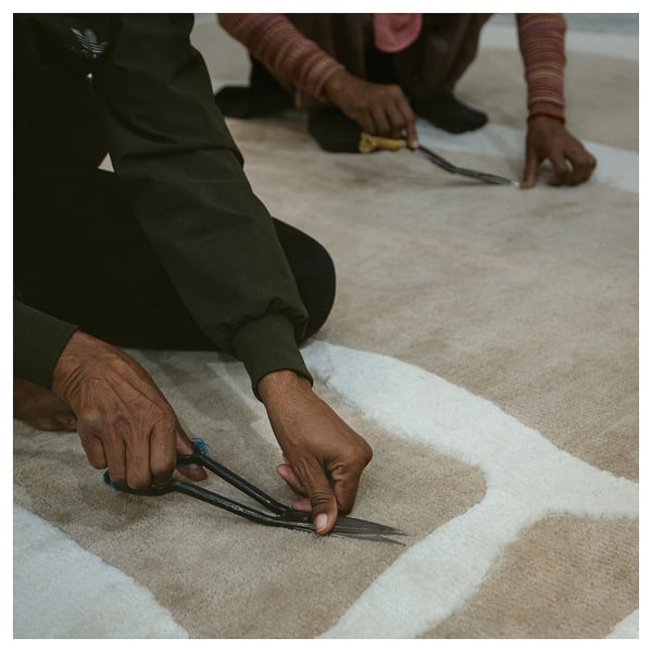 Two people trim white AXHAVREN rug, green pants.