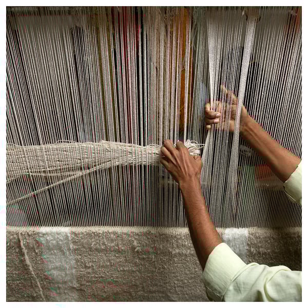 Person weaving on a loom, focusing on intricate pattern creation with threads.