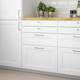 Modern white kitchen with AXSTAD drawer fronts. Smooth lines, inset panels, small drawers, plants, and wine.