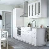 Modern white kitchen with AXSTAD cabinets, stainless fixtures, and glass doors, surrounded by light wood floors and a dining chair.