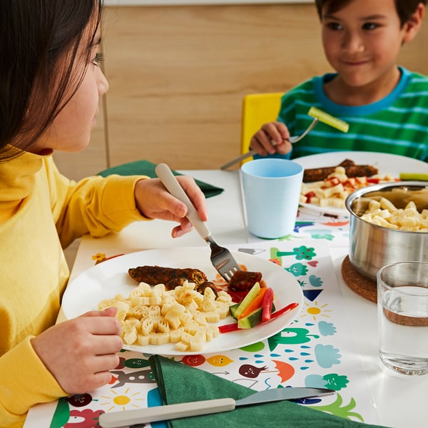Kids eating colorful meal, one in yellow, one in green striped shirt.