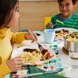 Kids eating colorful meal, one in yellow, one in green striped shirt.