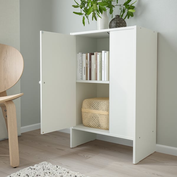 Small white BAGGEBO cabinet with doors, storing books and a basket, mounted against a light green wall.