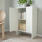 Small white BAGGEBO cabinet with doors, storing books and a basket, mounted against a light green wall.