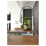 Modern kitchen with stainless steel faucet, broccoli in sink, wooden countertop.
