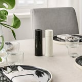 Modern table setting with black and white grinders, clear glasses, and stylish plates on beige tablecloth.