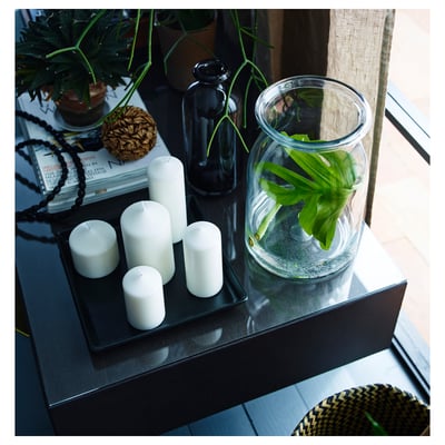 Black tray holds white candles, clear vase with green plant.