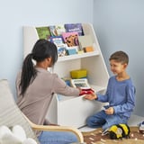 Woman assists boy using toy cash register at a child-sized bookcase with shelves and a drawer.