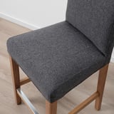 Close-up of a modern barstool, featuring a plush grey fabric seat and back, supported by sturdy wooden legs.