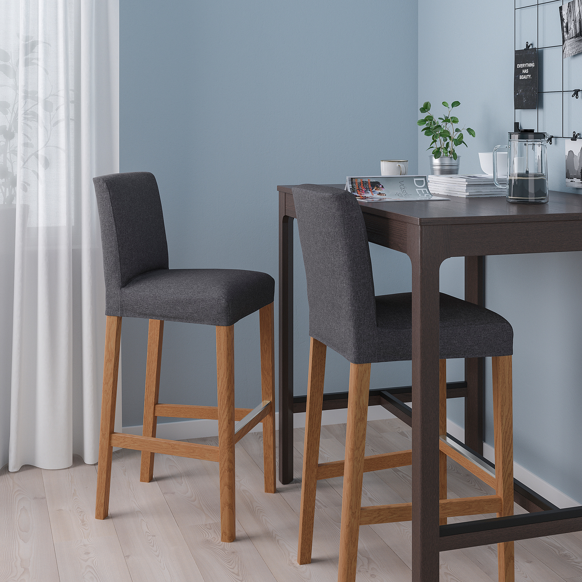 Modern bar stools, named BERGMUND, featuring grey, cushioned seats with wooden legs, positioned beside a high table; sleek and compact design.