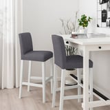 Two grey barstools with white legs and cushioned backs at a white table with plants and magazines.