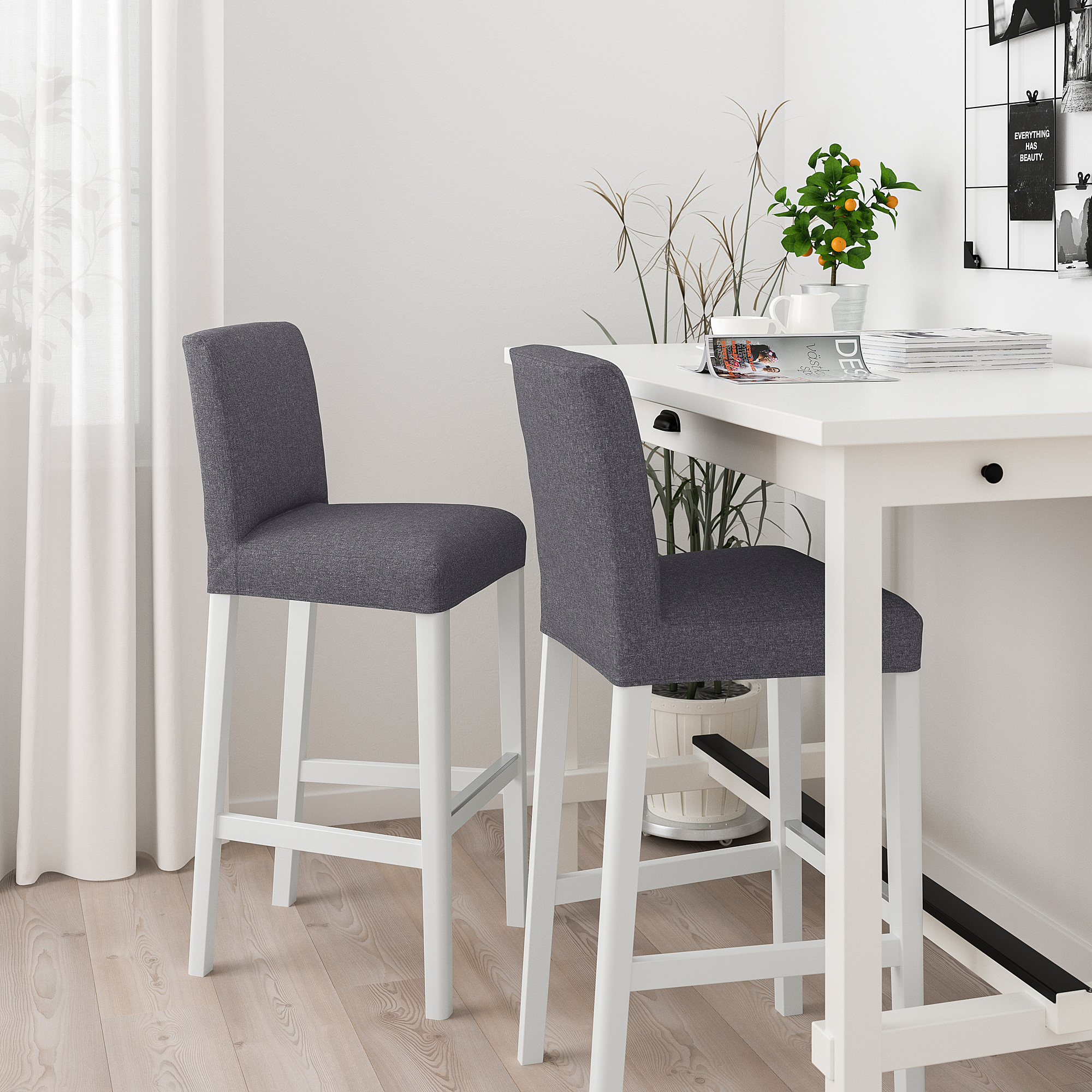 Two grey barstools with white legs and cushioned backs at a white table with plants and magazines.
