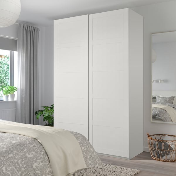 Modern minimalist bedroom with BERGSBO white closet, mirrored closet, bed with gray cover, plants, wicker basket.