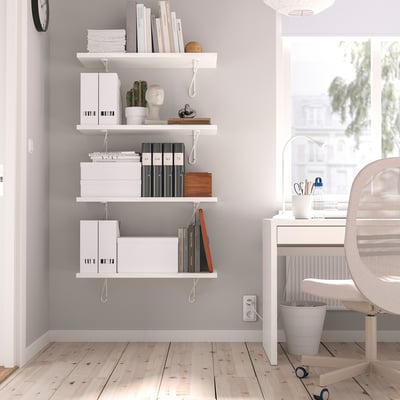 White BERGSHULT wall shelf with books, boxes, and decor. Mounted with two brackets, it fits neatly in the room corner above a desk.
