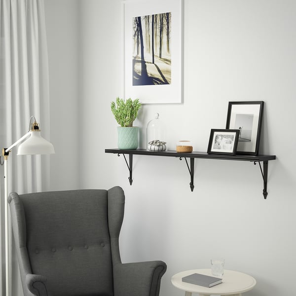 A cozy living area with a BERGSHULT black shelf holding a plant, decor, and a frame. Below, a table holds a book and a glass.