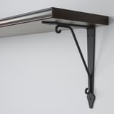 Dark metal shelf bracket with curved hooks attached to light-colored wall, supporting a dark wooden shelf.