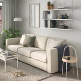 Modern living room with cream BERGSHULT sofa, wall shelf with books and plants, side table with remote and lamp.