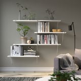 Minimalist living room with white shelf, books, plants, lamp, and couch.