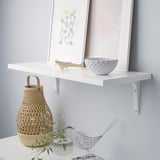 White wall shelf with wicker basket, small bowl, and framed art. Modern, multi-use display.