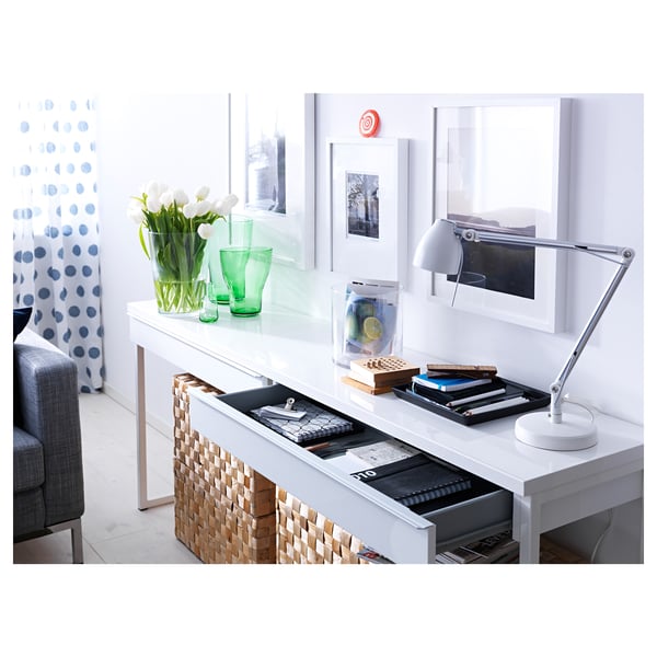 Modern white desk, sleek and stylish. Two drawers, a lamp, and green vases with white flowers. Cozy room decor.
