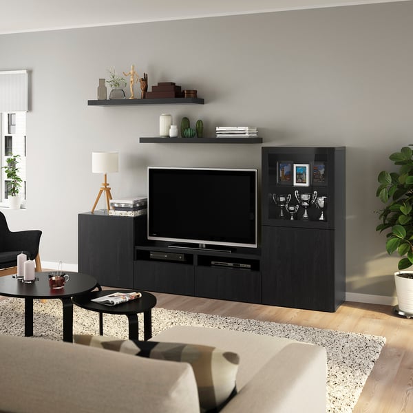 Modern living room with BESTÅ black tv unit, sofa, coffee table, rug, plants, white wall.