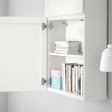 Open white cabinet with two shelves, holding stacks of books and boxes. Adjustable and customizable storage solution.